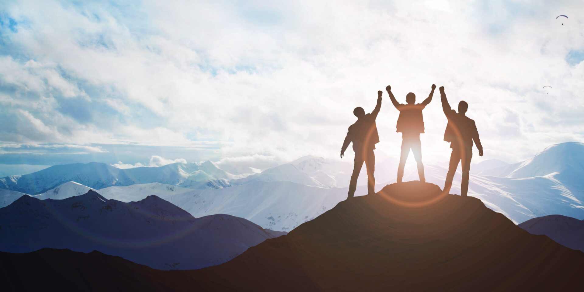 Photo of three people standing on a mountain holding their hands up