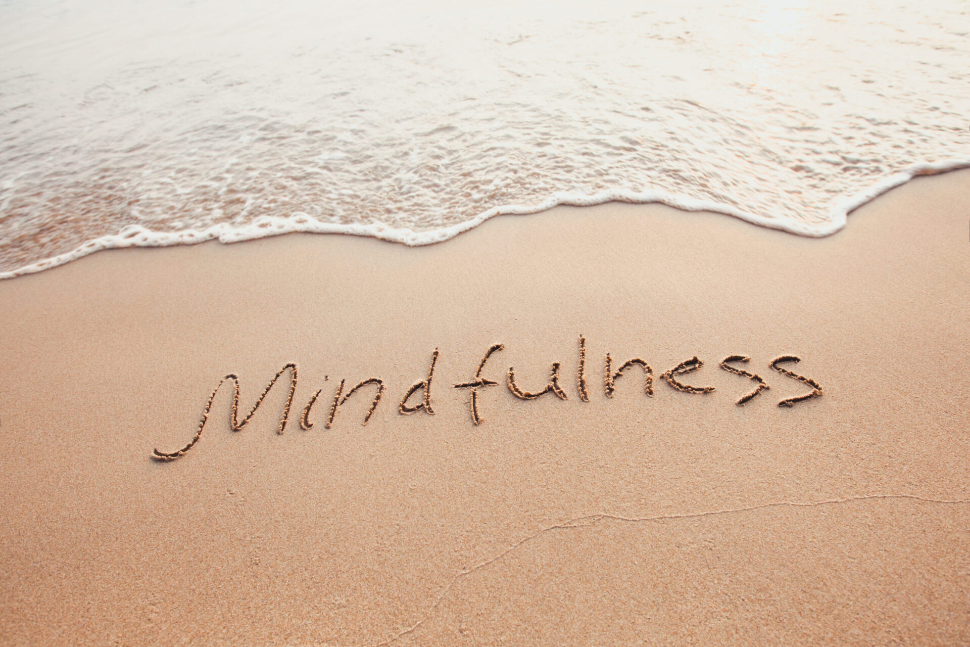 'Mindfulness' text written on the sand of beach