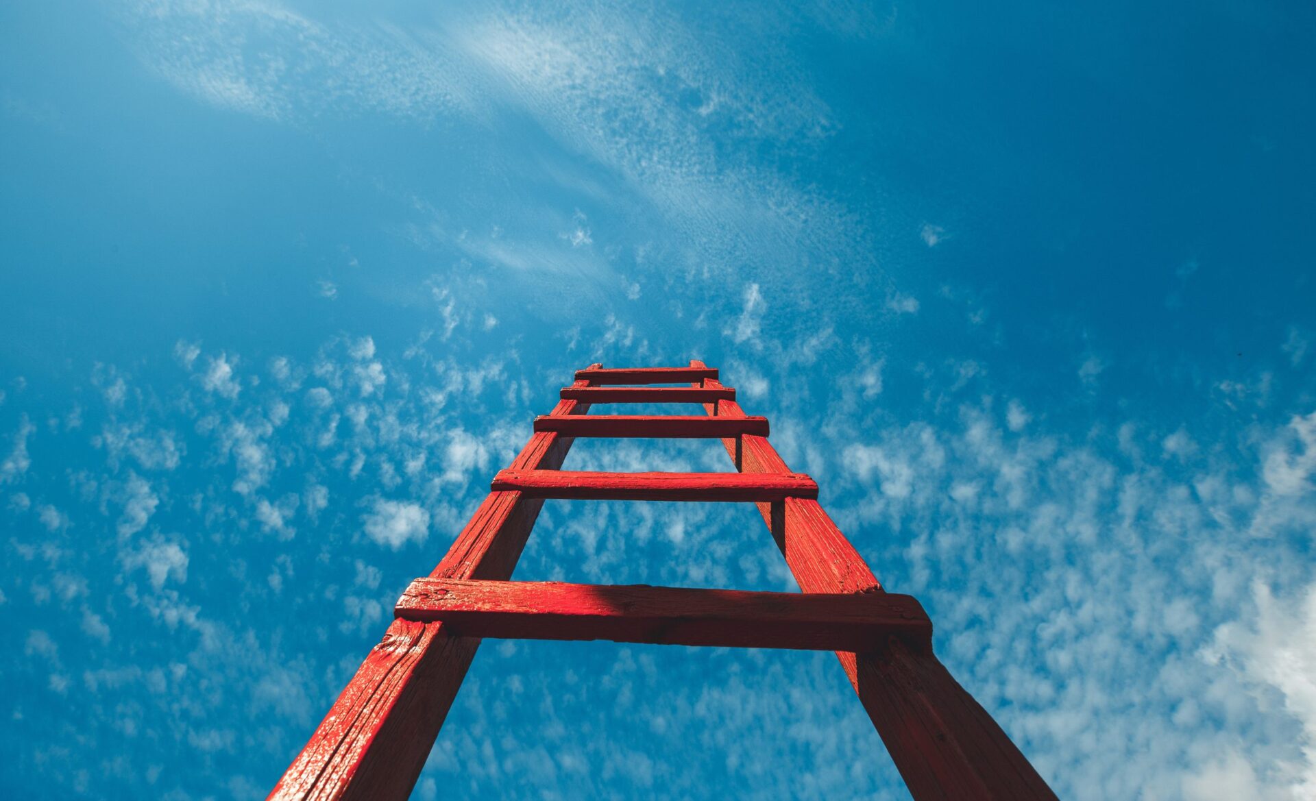 Photo of red ladder going upwards in a blue sky