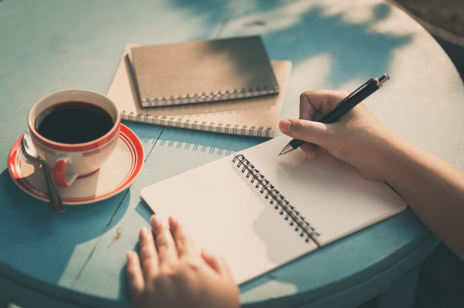 Photo of someone writing in a notebook with a cup of coffee