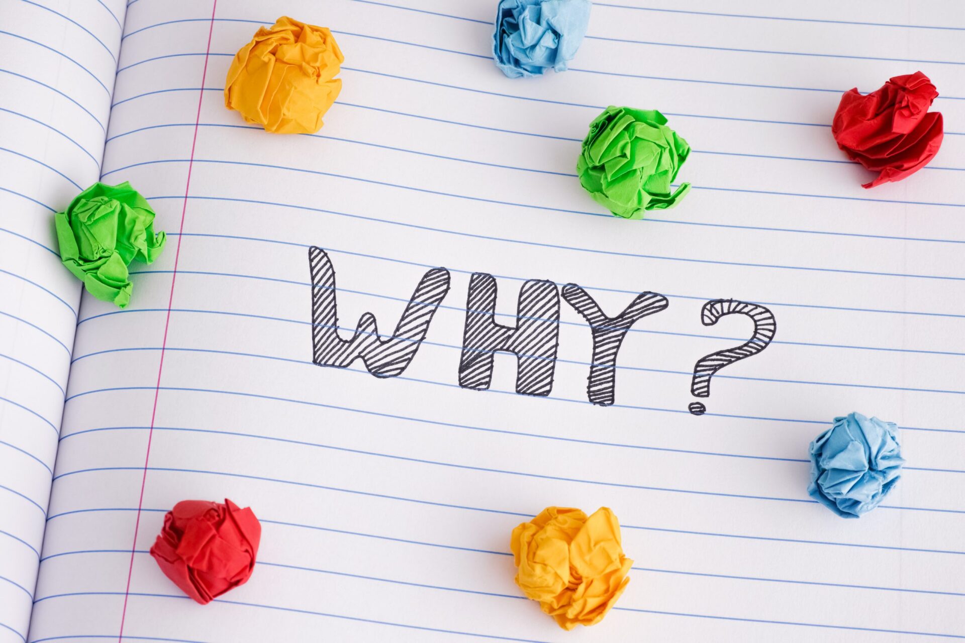 Photo of the word 'WHY?' written in a notepad surrounded by bits of coloured scrunched up paper