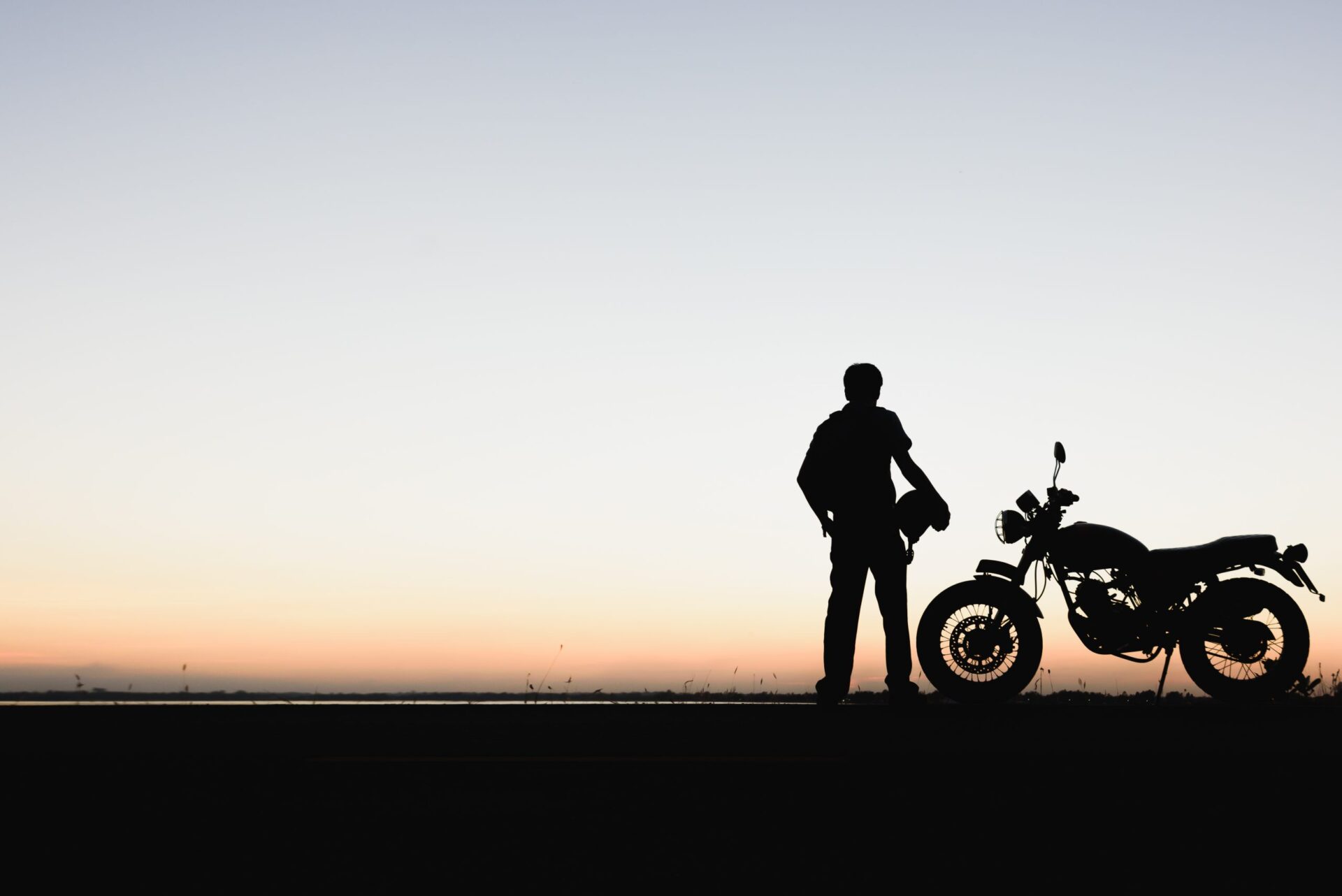 Photo of a silhouette of someone stood next to their motorbike